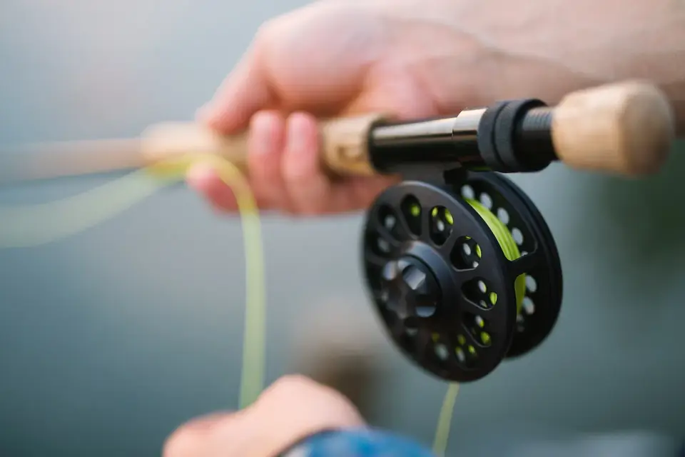Mãos a segurar uma cana de pesca à mosca com carreto preto e linha verde