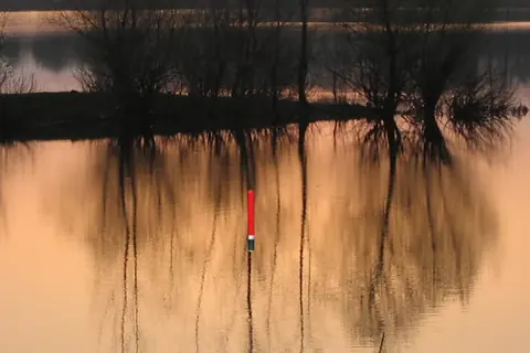 Float fishing simulator: bóia vermelha num lago ao pôr do sol, com árvores refletidas em tons de cobre