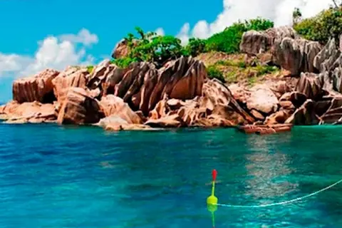 My Fishing World: ilha de rochas cor de salmão sobre água turquesa, com a bóia verde e vermelha em primeiro plano